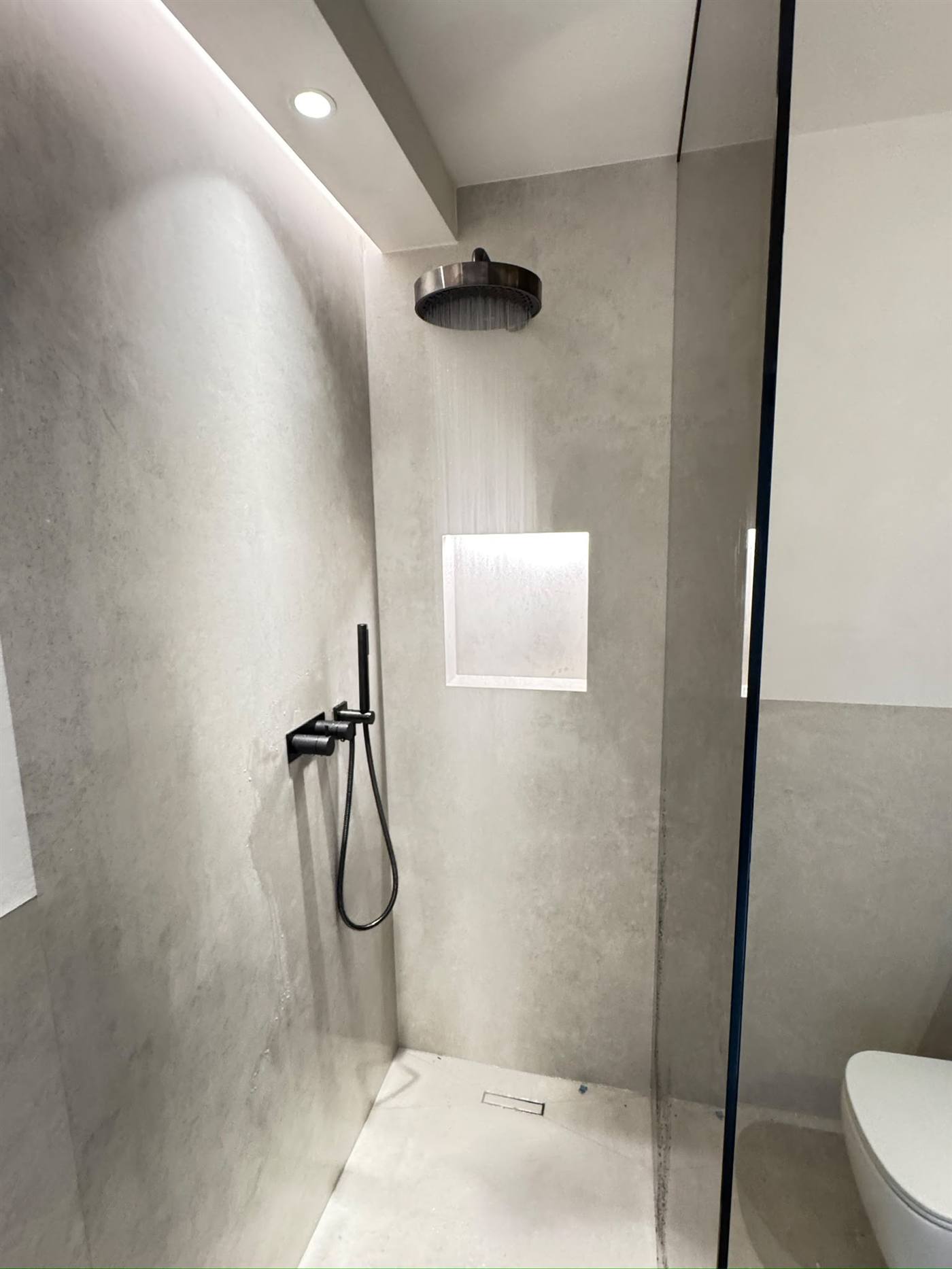 Fertig sanierte Dusche in Microzement-Optik mit schwarzen Armaturen